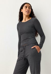 Maglia a maniche lunghe a righe bianche e nere abbinata a pantaloni a righe coordinati, caratterizzata da una vestibilità comoda e tasche laterali. Tessuto liscio.