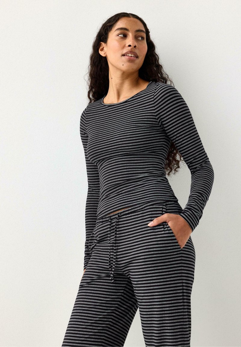 Maglia a maniche lunghe a righe bianche e nere abbinata a pantaloni a righe coordinati, caratterizzata da una vestibilità comoda e tasche laterali. Tessuto liscio.