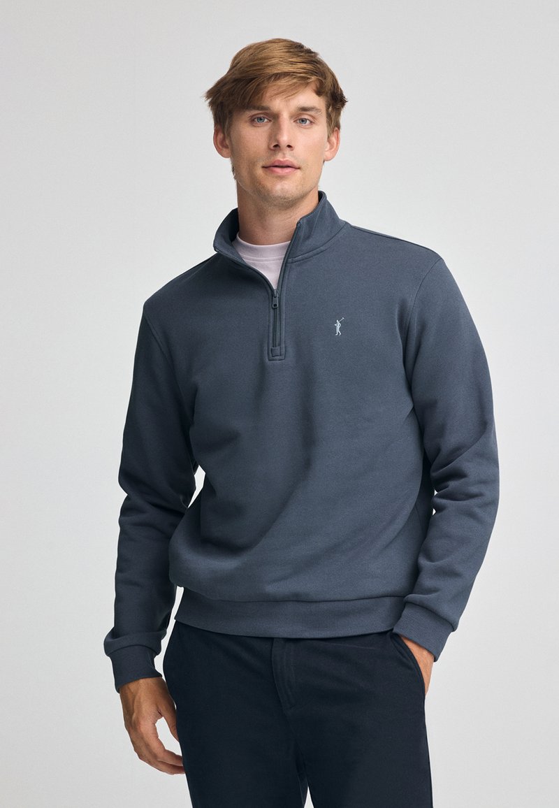 Grå fleecepullover med dragkedja i kragen och broderad logotyp på bröstet. Har ribbade muddar och nederkant, samt en mjuk yta.