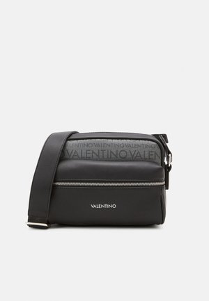 Black leather crossbody bag with a zip closure and adjustable strap. Features embossed branding on the top and metallic hardware accents.