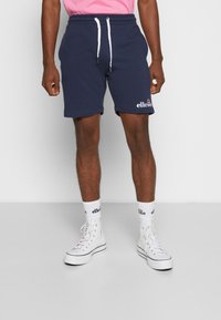 Marineblaue Sweat-Shorts mit elastischem Bund und weißem Kordelzug. Mit gesticktem Logo in Weiß. Trägt man mit weißen hohen Sneakers und Socken.