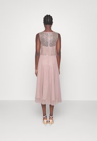 Kvällsklänning med en paljettprydd överdel och en flödande, enfärgad ljusrosa kjol. Styld med remklackar och med en lager-på-lager design.