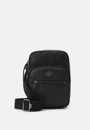 Borsa a tracolla nera con motivo geometrico testurizzato, tasca frontale con zip e tracolla regolabile. Logo Lacoste presente sul fronte.