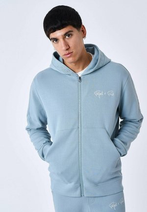 Lichtblauwe rits-hoodie van zachte stof, met voorzakken, geborduurd logo en capuchon met trekkoord. Glad oppervlak, normaal model.