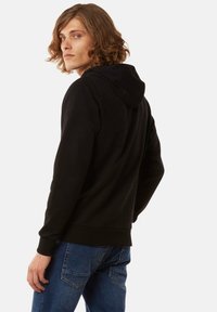 Sudadera negra con bolsillo canguro en la parte frontal y capucha con cordón, hecha de una tela texturizada. Combinada con jeans de mezclilla azul.