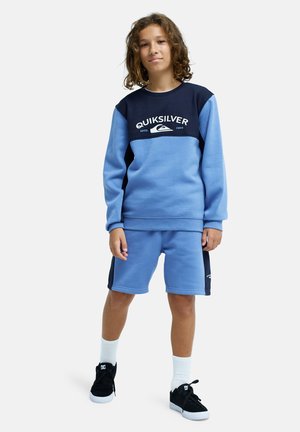 Light blue sweatshirt with navy accents and logo, paired with matching shorts. Material appears soft; outfit suitable for casual wear.