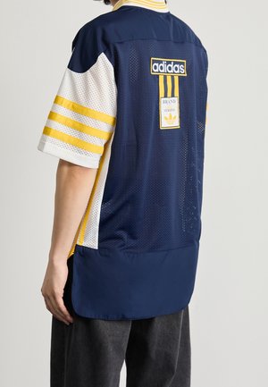 Personne portant un maillot en mesh Adidas à manches courtes bleu marine et blanc avec des bandes jaunes et des logos de marque visibles dans le dos.