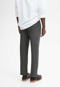 Gray trousers made of a smooth fabric, featuring a straight-leg design and two back pockets, paired with black shoes and a white shirt.
