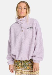 Licht lavendel kleurige pullover gemaakt van pluizige, gestructureerde stof. Heeft een hoge kraag, drie houten knopen en een klein geborduurd logo.