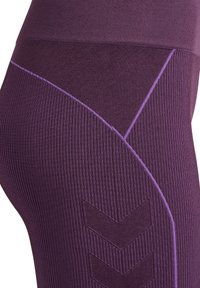 Paarse leggings met ribbeltextuur, met contrasterende dunne paarse stiksels en een chevronpatroonaccent op het onderbeen.