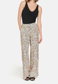 Pantalons larges avec une base beige, présentant un motif à pois noirs. Le tissu est lisse, avec une coupe ample et des poches latérales.