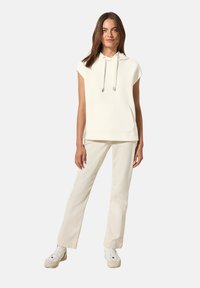 Haut à capuche crème à manches courtes avec cordons de serrage et poche avant, associé à un pantalon beige clair et des baskets blanches. Design minimaliste.