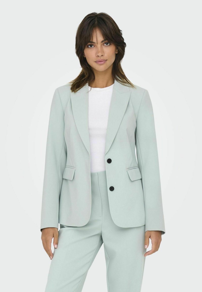 Blazer vert menthe clair et pantalon assorti, avec deux poches avant, des revers à cran et des boutons noirs. Coupe lisse et ajustée.