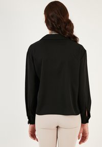 Blusa nera a maniche lunghe con una vestibilità rilassata, dotata di colletto classico e polsini con bottone. Tessuto liscio e leggero.