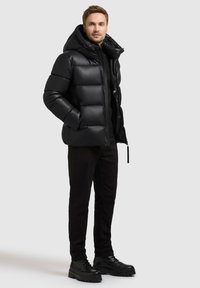 Giubbotto imbottito nero con ampie sezioni trapuntate, cappuccio e chiusura con zip, abbinato a pantaloni neri e stivaletti neri robusti.