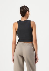 Black ribbed crop tank top paired with light taupe sweatpants featuring an elastic waistband, providing a relaxed silhouette.