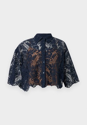 Blouse courte en dentelle bleu marine avec motif floral, boutonnage à l'avant, col et manches larges à bords festonnés.