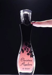 Un dito con unghie smaltate di rosso tocca la parte superiore di una bottiglia rosa del profumo Christina Aguilera By Night decorata con motivi floreali neri.