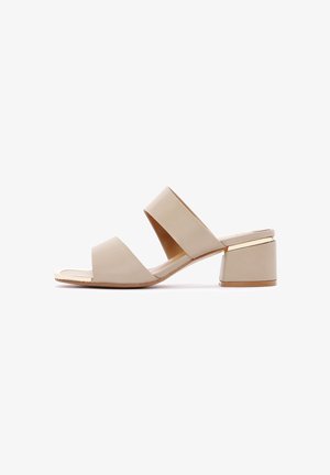 Sandale à talon block ouvert beige avec deux larges brides et un accent doré sur le talon. Matériau lisse et surface légèrement texturée.