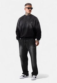 Schwarzer, übergroßer Pullover mit einem dezenten Farbverlauf; kombiniert mit schwarzen Jeanshosen mit ausgefransten Taschen und einer lässigen Passform.