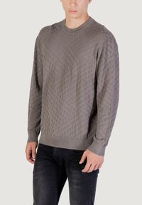 Pull en maille texturée gris avec un motif géométrique, doté d'un col rond et de poignets côtelés, associé à un jean foncé.