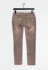 Hnědé, upnuté džínové kalhoty visící na černém ramínku. Mají pět kapes, zip a jemně vybledlou texturu na látce.