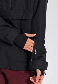 Giacca nera impermeabile con collo alto e taschino sul petto con zip. Caratterizzata da polsini elasticizzati con dettagli del logo e orlo regolabile.