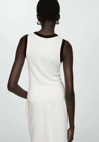 Sleeveless sweater in white knit with a brown trim around the neckline. Features a fitted design, ribbed texture, and no visible fastenings.