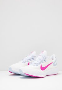 Scarpe atletiche bianche Nike con accenti rosa, dotate di una tomaia in mesh, suola testurizzata e dettagli azzurri chiari sui lati e sui lacci.