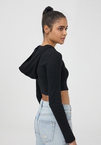 Felpa nera a maniche lunghe, corta, con cappuccio e coulisse, in tessuto a costine, abbinata a jeans chiari strappati a vita alta.