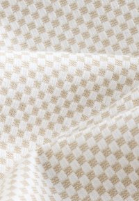 Tissu tissé présentant un motif à carreaux beige et crème, avec une texture douce et des carrés alternés distincts.