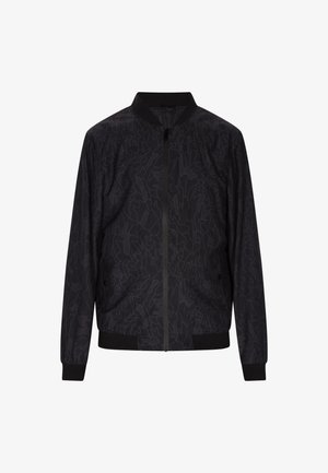 Melna bomber jakne ar smalku abstraktu rakstu, ribainiem piedurknēm un apkakli, ar rāvējslēdzēja aizdari un divām sānu kabatām. Izgatavota no viegla auduma.