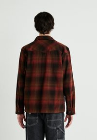 Camicia a quadri rossa e nera con colletto a punta, maniche lunghe e polsini con bottone; presenta una trama tessuta e una vestibilità comoda.