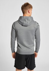 Grijze hoodie voor heren met een aansluitend ontwerp, lange mouwen en een trekkoordkap, met zwarte accenten op de schouders en een soepele textuur.