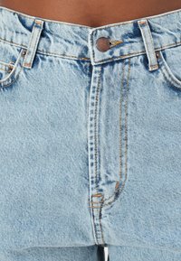 Gai zili džinsi īsās bikses ar augstu jostasvietu, ar varšiem pogām, oranžām diegu šuvēm un nedaudz izbalējušu tekstūru.