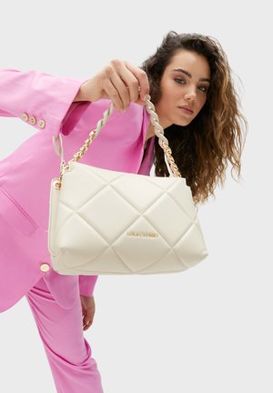 Bolso de mano acolchado en crema con una correa de cadena trenzada y herrajes dorados. El bolso presenta un sutil logo en relieve en la parte frontal.