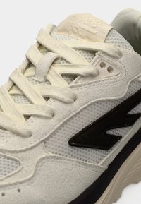 Baskets gris clair avec tige en mesh, accents en daim et logo gris foncé. Les lacets sont plats et légèrement texturés avec une semelle rembourrée.