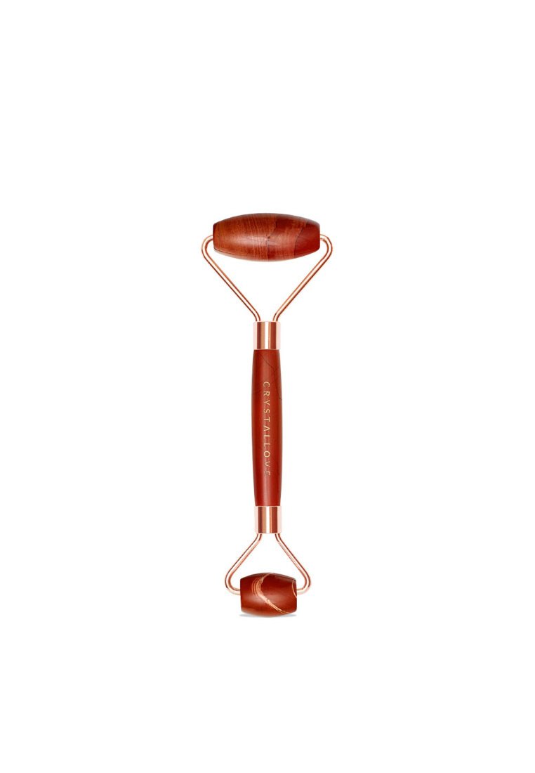 Red jade facial roller with a sturdy, rose gold metal frame. Features two rolling stones: one larger and oval, one smaller and round.