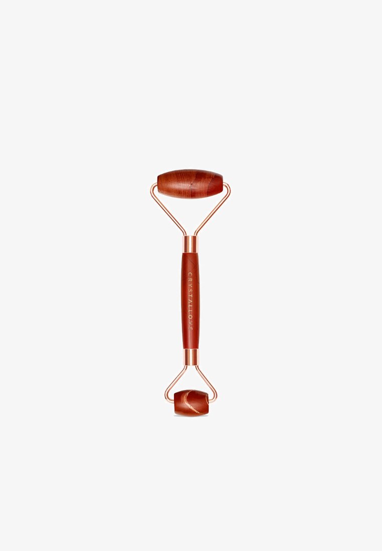 Rullo facciale in giada rossa con una robusta cornice in metallo color oro rosa. Presenta due pietre rotolanti: una più grande e ovale, l'altra più piccola e rotonda.