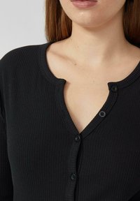 Zwarte, geribbelde, gebreide cardigan met een V-hals en twee zwarte knopen aan de voorkant. De textuur oogt zacht en aansluitend.