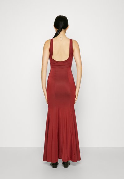 Dlhé, priliehavé vínovočervené šaty s hladkou textúrou, hlbokým výstrihom na chrbte a rozšíreným lemom. Modelka má obuté čierne podpätky; vlasy má upravené do vrkoča.