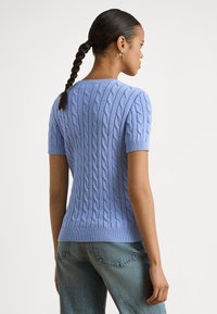 Svetlo modra pletena majica s kratkimi rokavi, z vzorcem kabelske pletenine in rebrastim spodnjim robom, kombinirana z visokim pasom kavbojk iz jeansa.