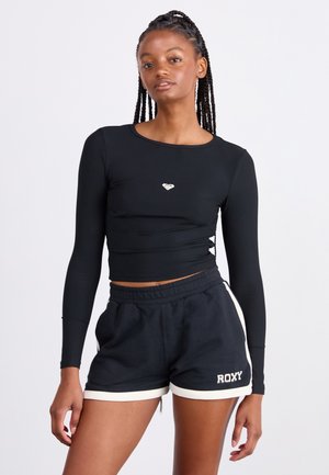 Black ribbed long-sleeve top with a fitted design and small heart logo at the center, paired with black shorts featuring white accents.