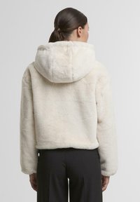 Cremfarbener Kunstpelz-Jacke mit Kapuze, cropped Design und langen Ärmeln, mit einer weichen Textur und ohne sichtbare Hardware-Details.
