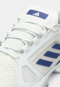 Chaussure de sport blanche avec tissu en mesh, lacets blancs, bandes du logo Adidas bleues et patch du logo bleu sur la languette.