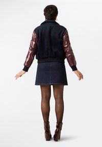 Svart och burgundy bomberjacka med glänsande ärmar, ribbade manschetter och en mysig textur. Kombinerad med en mörk denimkjol och glänsande ankelskor.