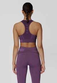 Fioletowy sportowy stanik i pasujące legginsy z teksturowanej tkaniny. Stanik ma fason z plecami typu racerback oraz kontrastowe szwy; logo na pasku.