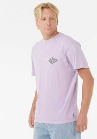 Camiseta de algodón morada con cuello redondo y mangas cortas. Presenta un pequeño diseño gráfico negro en el pecho. Corte casual.