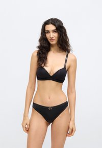 Fekete melltartó mély dekoltázzsal és állítható pántokkal, logóval díszítve. Fekete bikini alsó csipkés részlettel. Simább anyag, minimális díszítés.