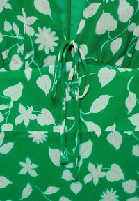 Rochie verde cu un model floral alb. Include o curea la talie, un fermoar la spate și un material ușor, texturat.